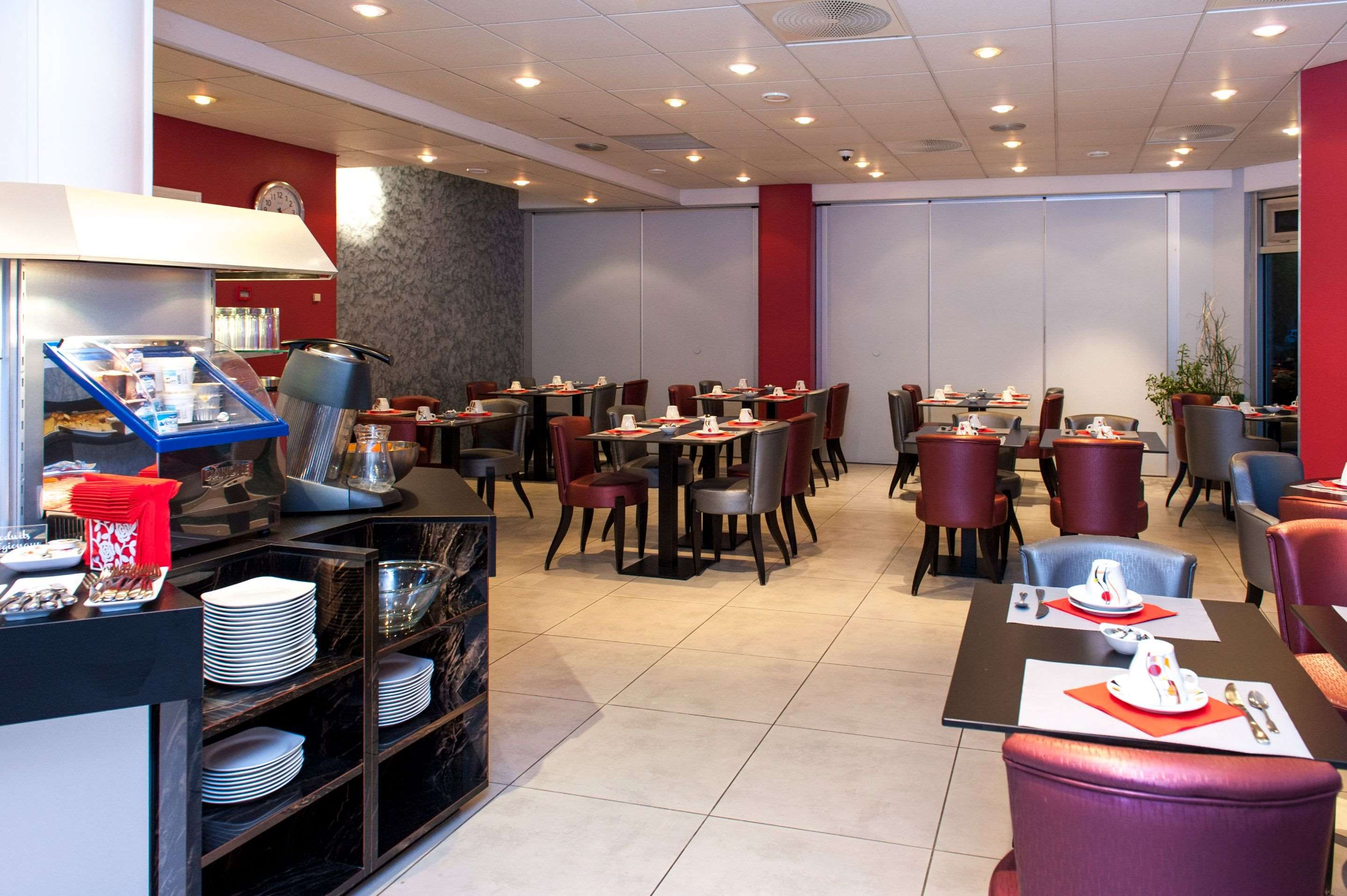 Une salle à manger d’hôtel avec plusieurs tables et chaises, un buffet proposant une variété de plats et de boissons, et une horloge au mur.