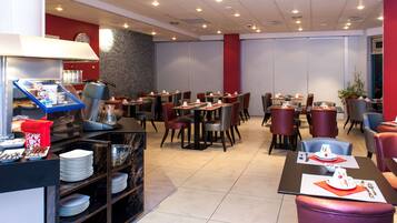 Une salle à manger d’hôtel avec plusieurs tables et chaises, un buffet proposant une variété de plats et de boissons, et une horloge au mur.