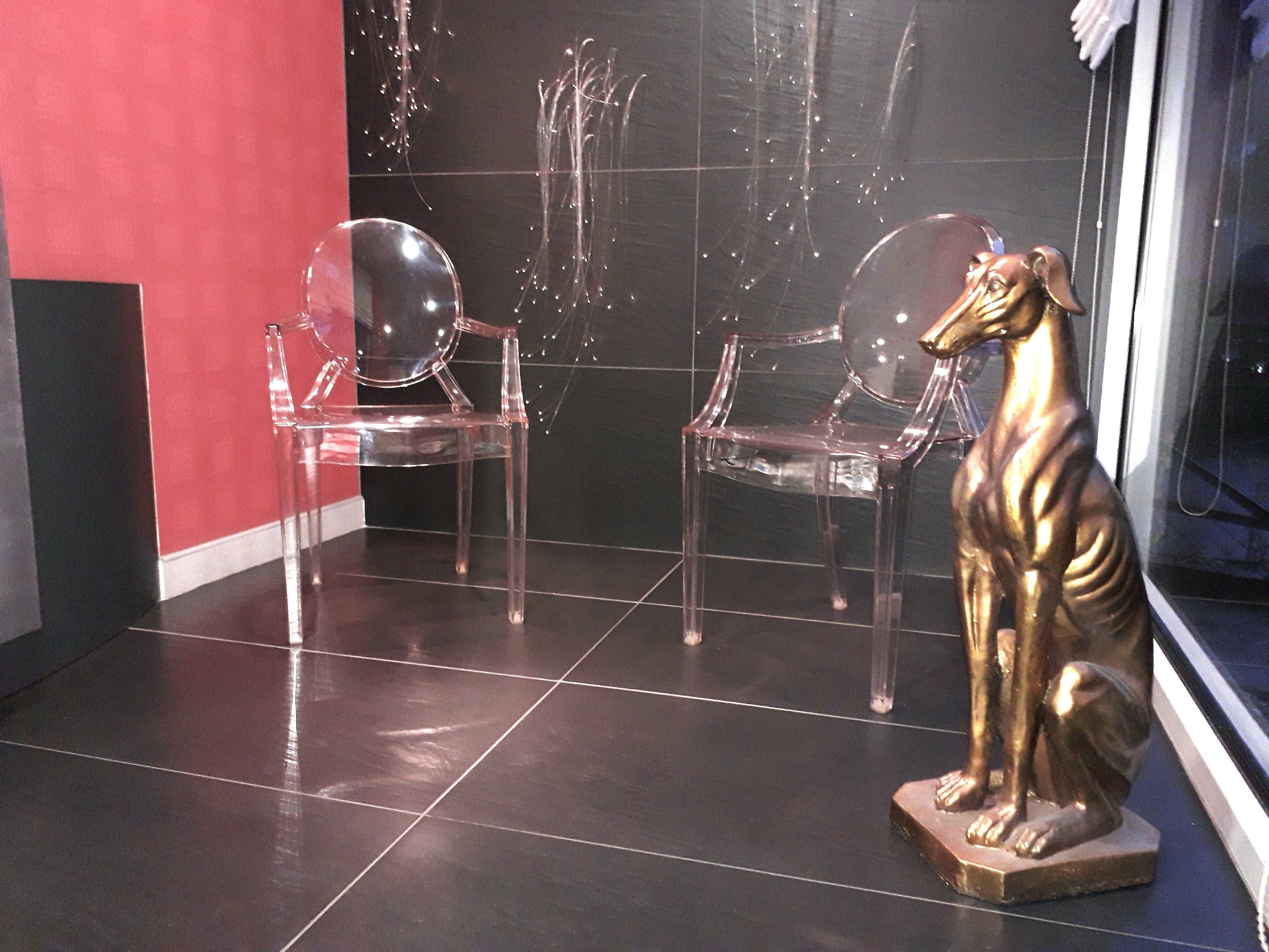 Una habitación con dos sillas de plástico transparente y una estatua dorada de un perro.