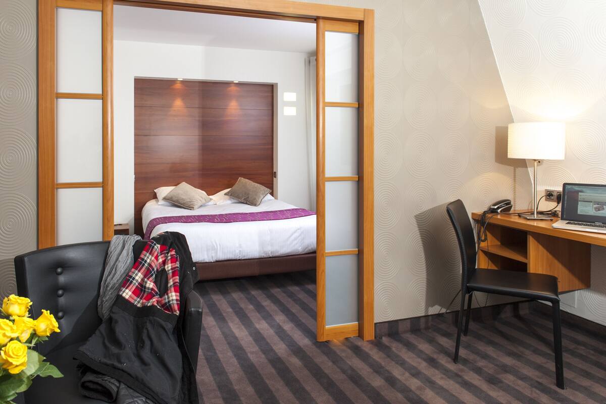 Una habitación de hotel con una cama, un escritorio con computadora, una silla y una lámpara.