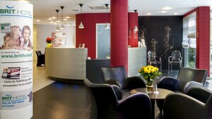 Zona de recepción de un hotel con una decoración en rojo y negro, una mesa de recepción y varias áreas de descanso con mesas y sillas.