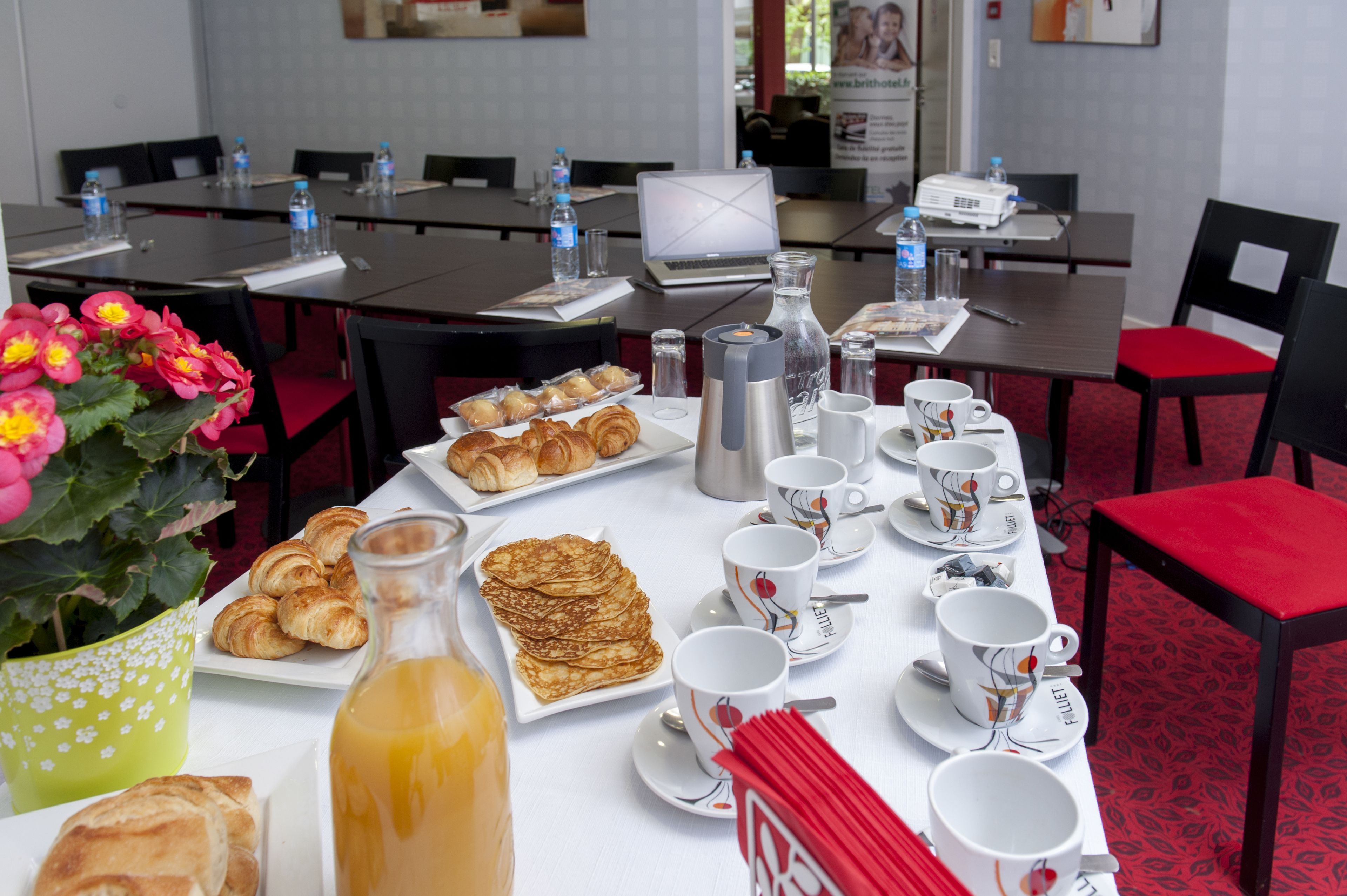 Ein Frühstückstisch mit Croissants, Gebäck und Saft, im Hintergrund Wasserflaschen und ein Laptop.