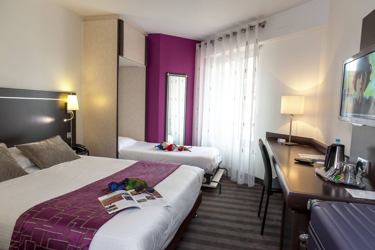 Habitación de hotel con dos camas, un escritorio, una silla, un televisor y una ventana con cortinas.