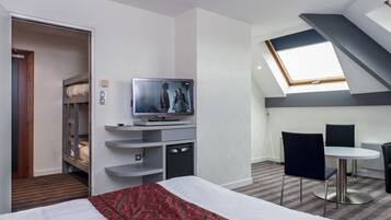 Una habitación de hotel con cama, televisión, escritorio con sillas, tragaluz y armario.