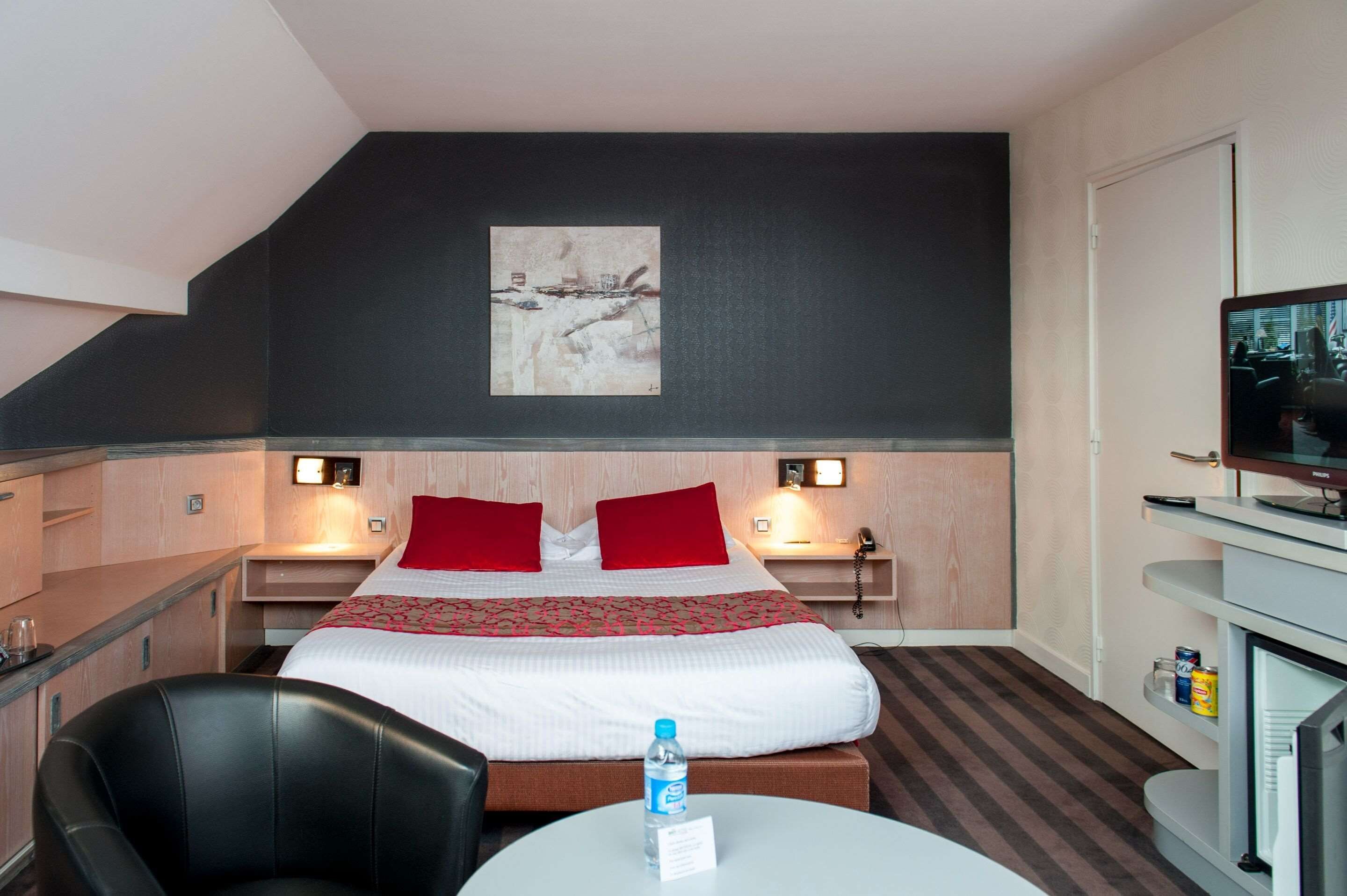 A hotel room with a bed, a desk, a chair, a television, and a painting on the wall.