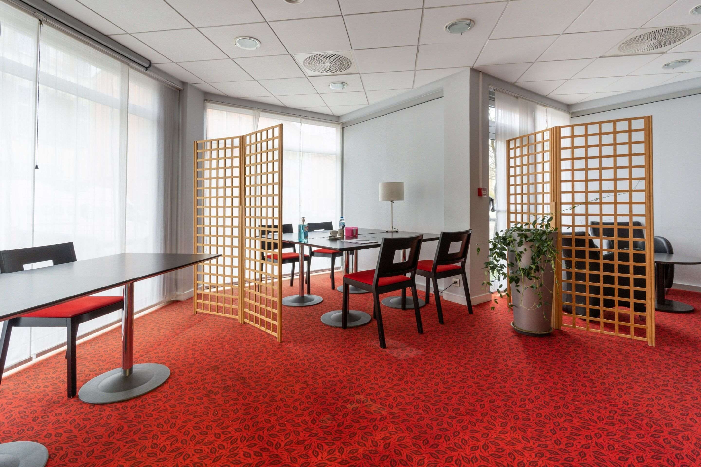 Un salón de conferencias con alfombra estampada de color rojo, separadores de madera y una planta en maceta.