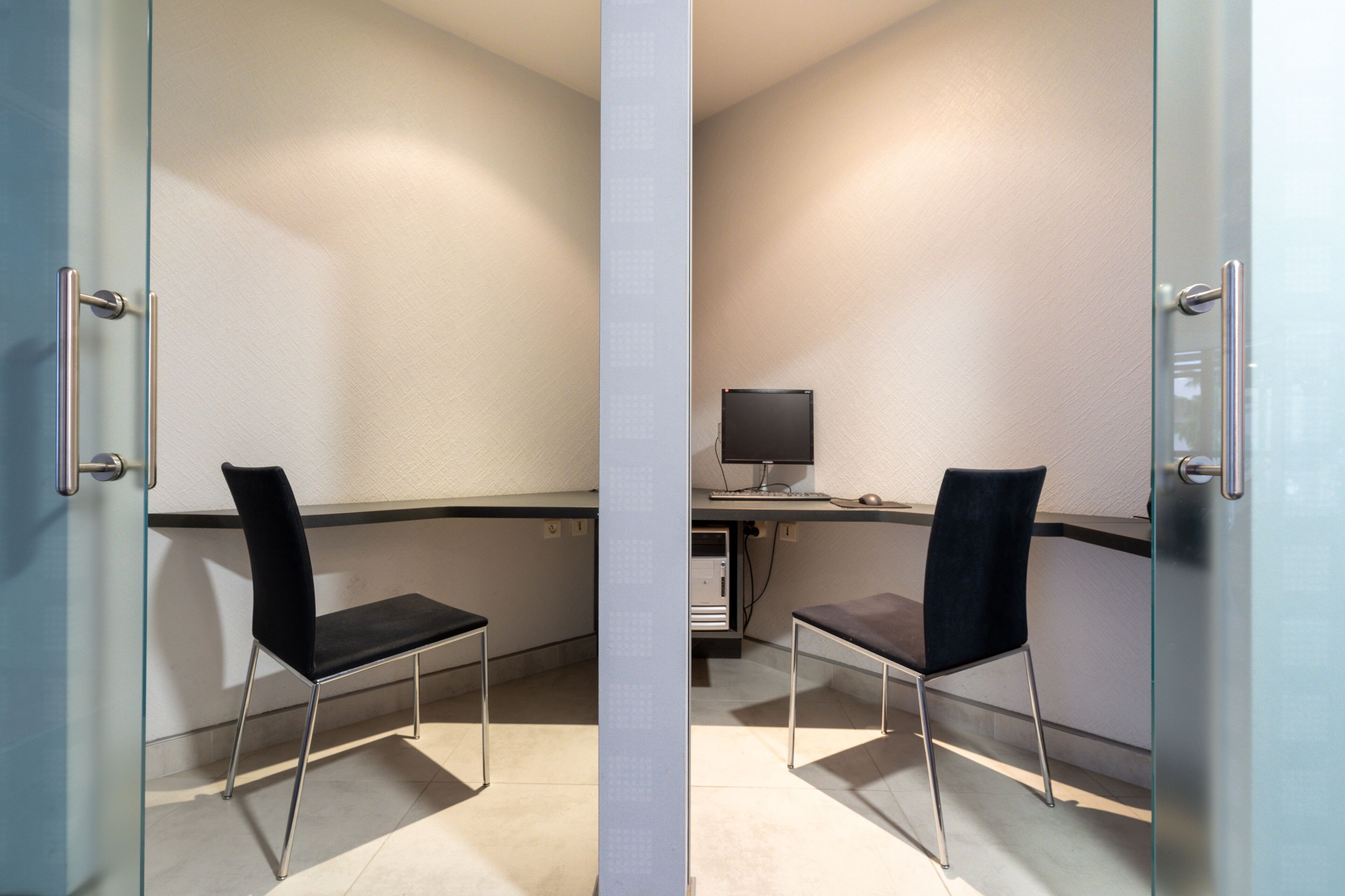 Un espace de bureau moderne avec deux chaises noires, un bureau avec un ordinateur et une cloison en verre.