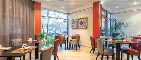 Un restaurante moderno con varias mesas y sillas, ventanas amplias y vistas al exterior.