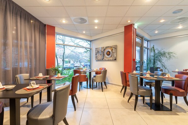 Un restaurante moderno con varias mesas y sillas, ventanas amplias y vistas al exterior.