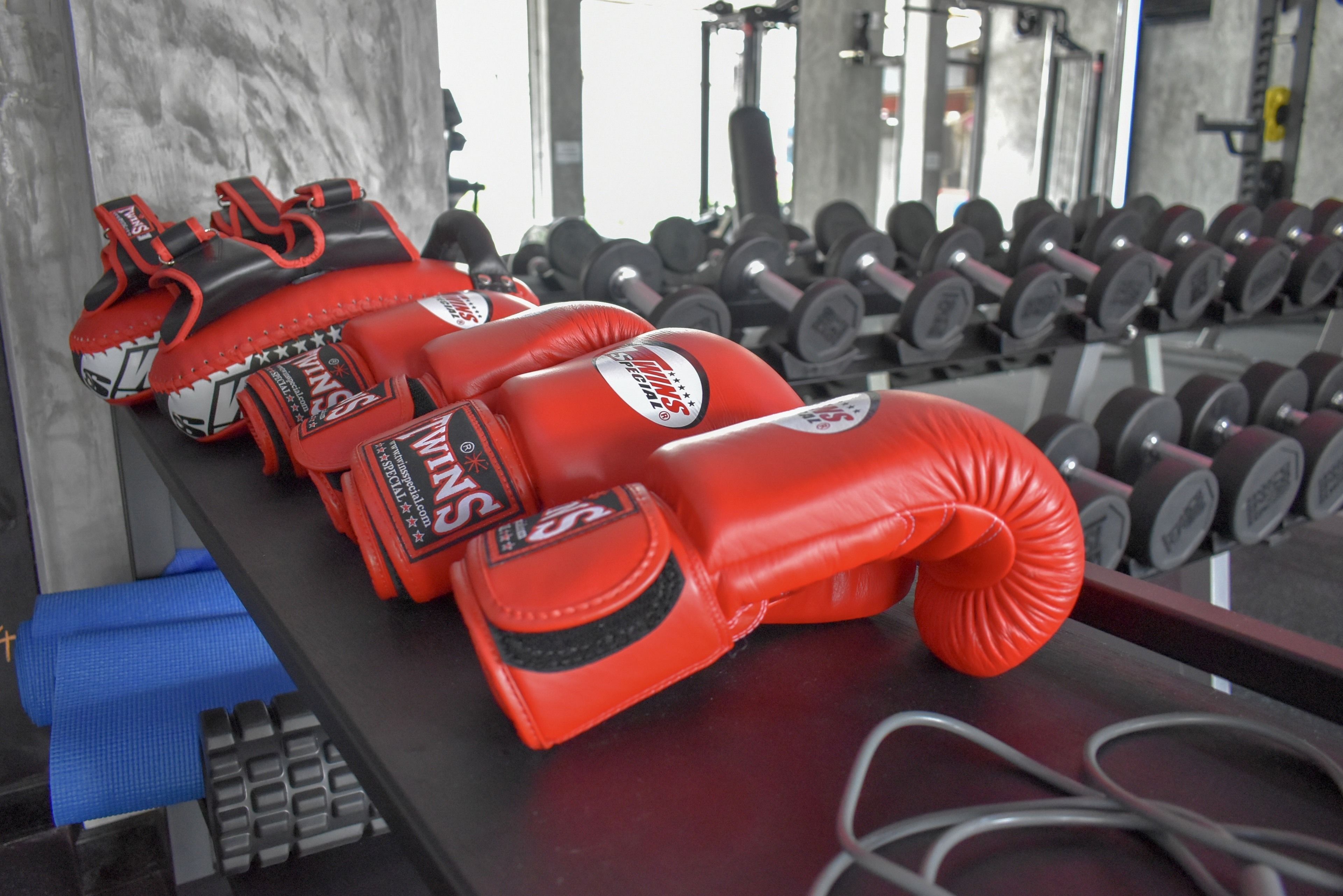 Una fila de guantes de boxeo rojos sobre una barra en un gimnasio, con mancuernas al fondo.