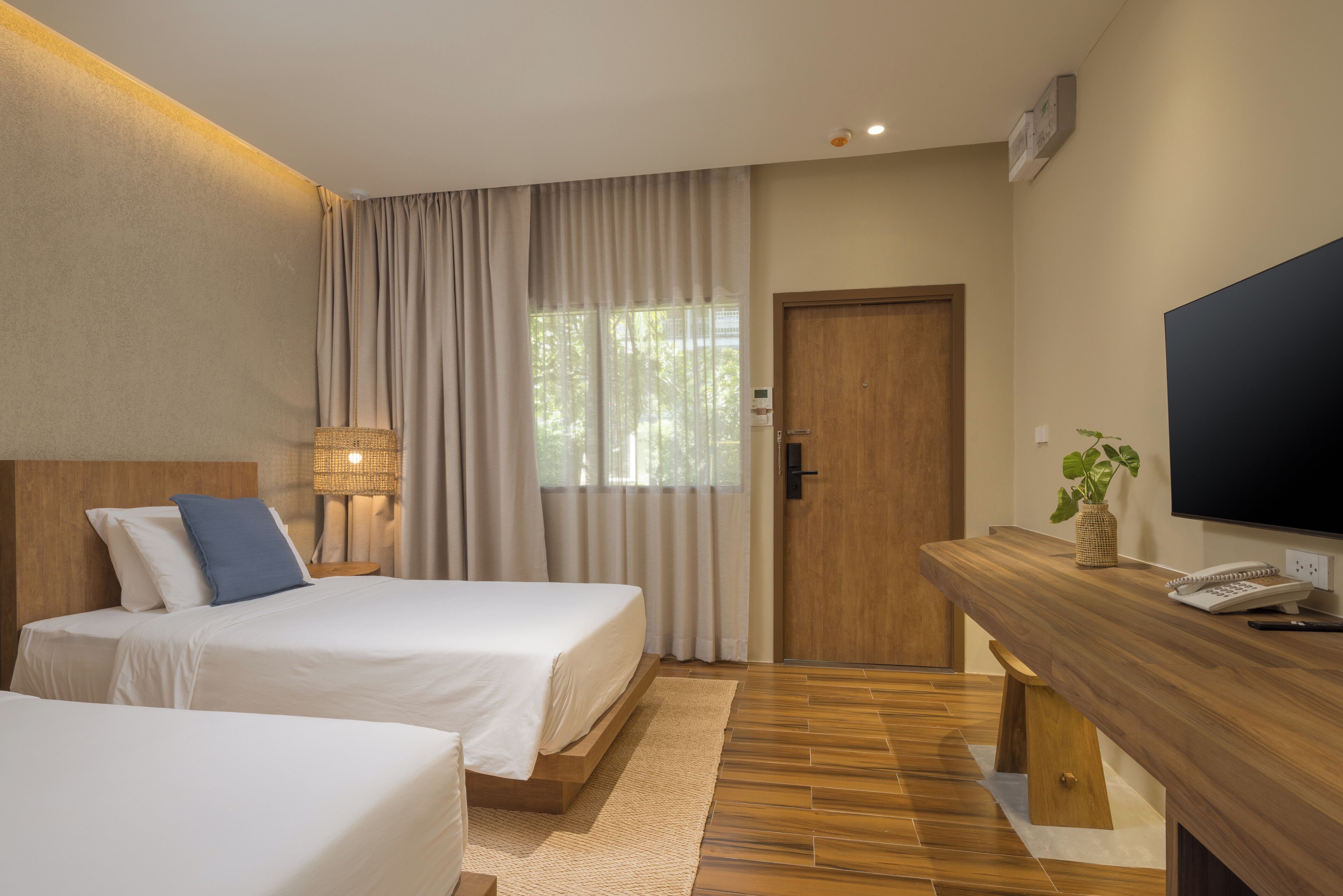 A hotel room with two beds, a wooden desk, a television, and a window with curtains.