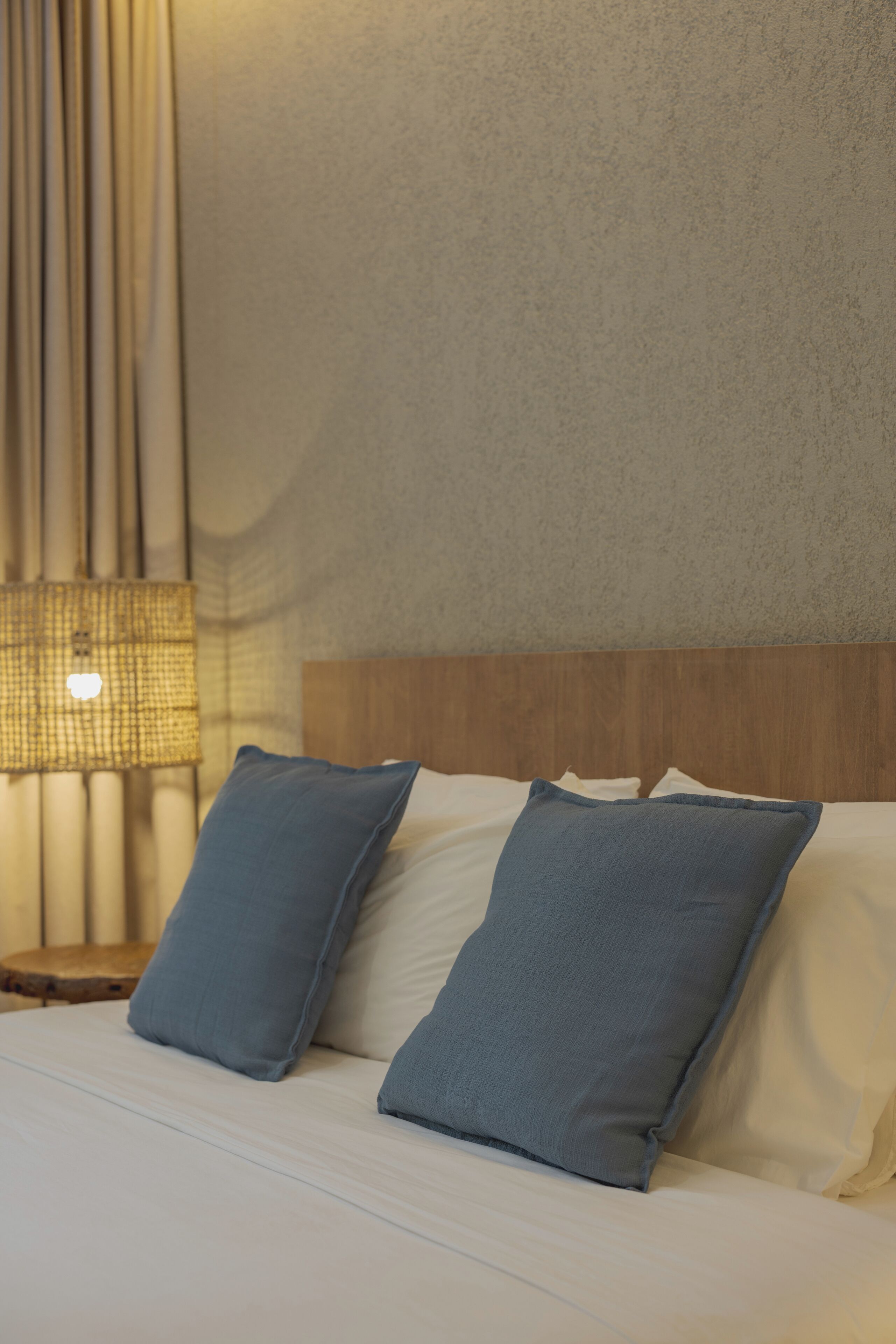 Una cama bien hecha con dos almohadas, un cabecero de madera y una lámpara en una mesita de noche.