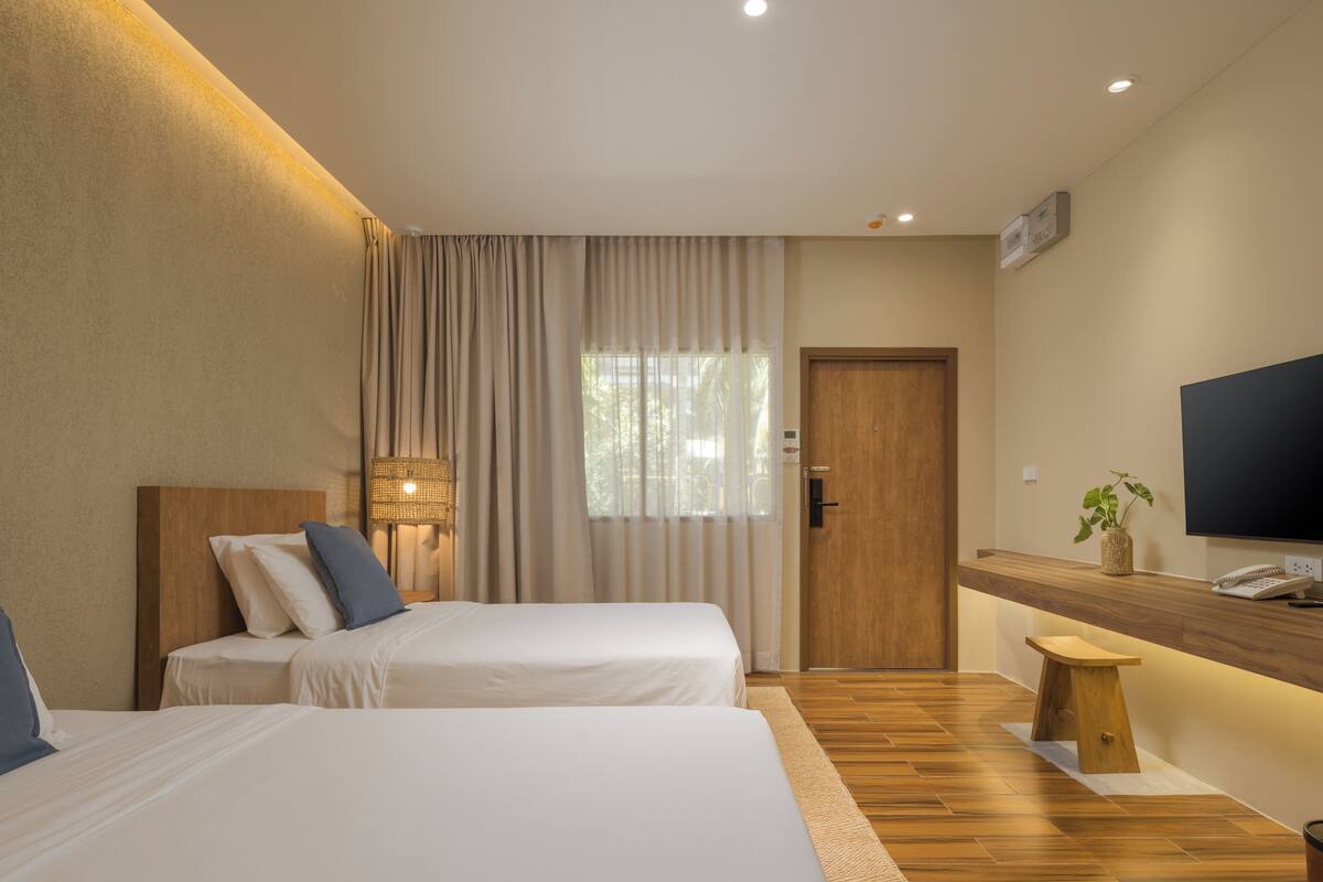 Een hotelkamer met twee bedden, een houten vloer, een televisie en een klein krukje.