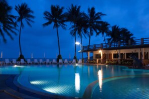 A swimming pool with lounge chairs and palm trees, surrounded by a building with a balcony.