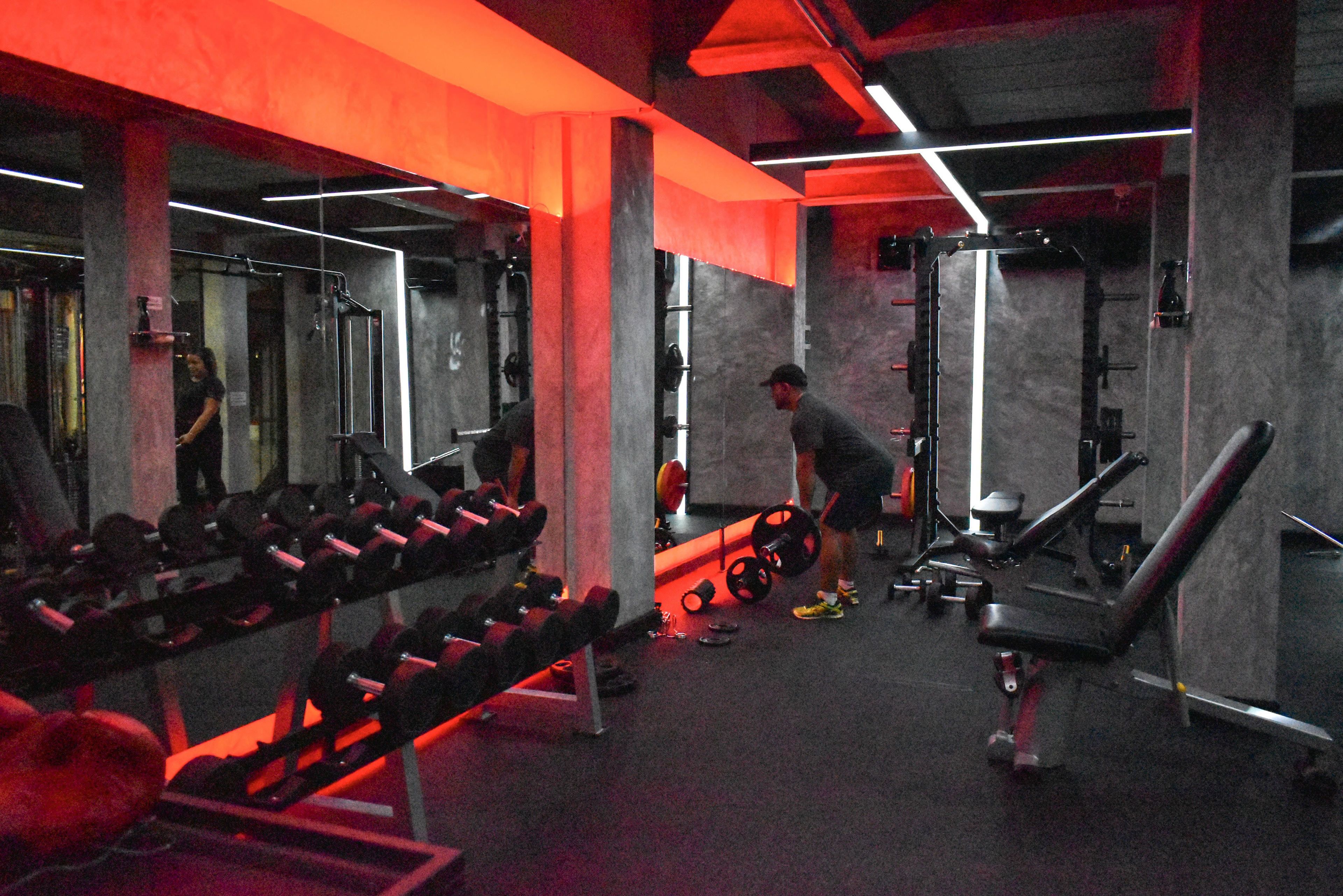 Un gimnasio con equipo de levantamiento de pesas, bancos y un espejo grande.