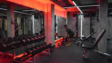 Un gimnasio con equipo de levantamiento de pesas, bancos y un espejo grande.