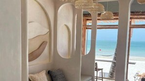Una habitación junto a la playa con sofá, una mesita y otomanas de mimbre.