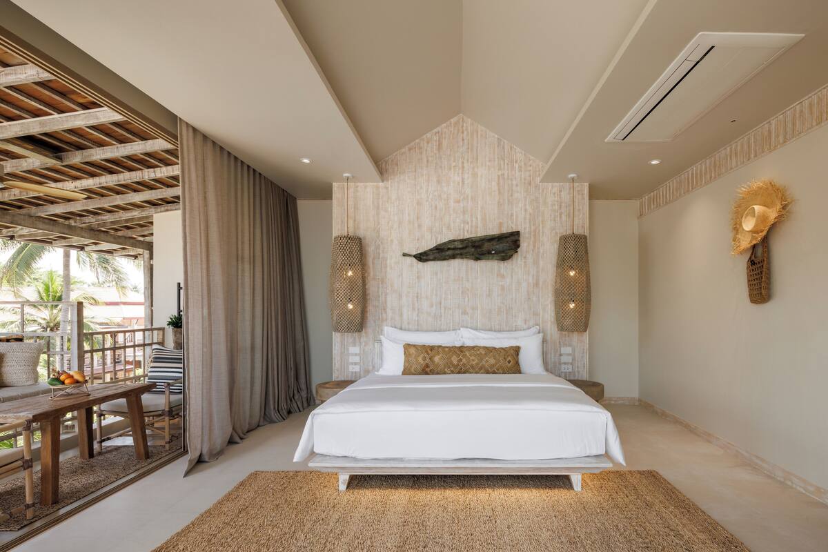 Een slaapkamer met een bed, een houten bankje, een tafeltje met fruit en uitzicht op het landschap.