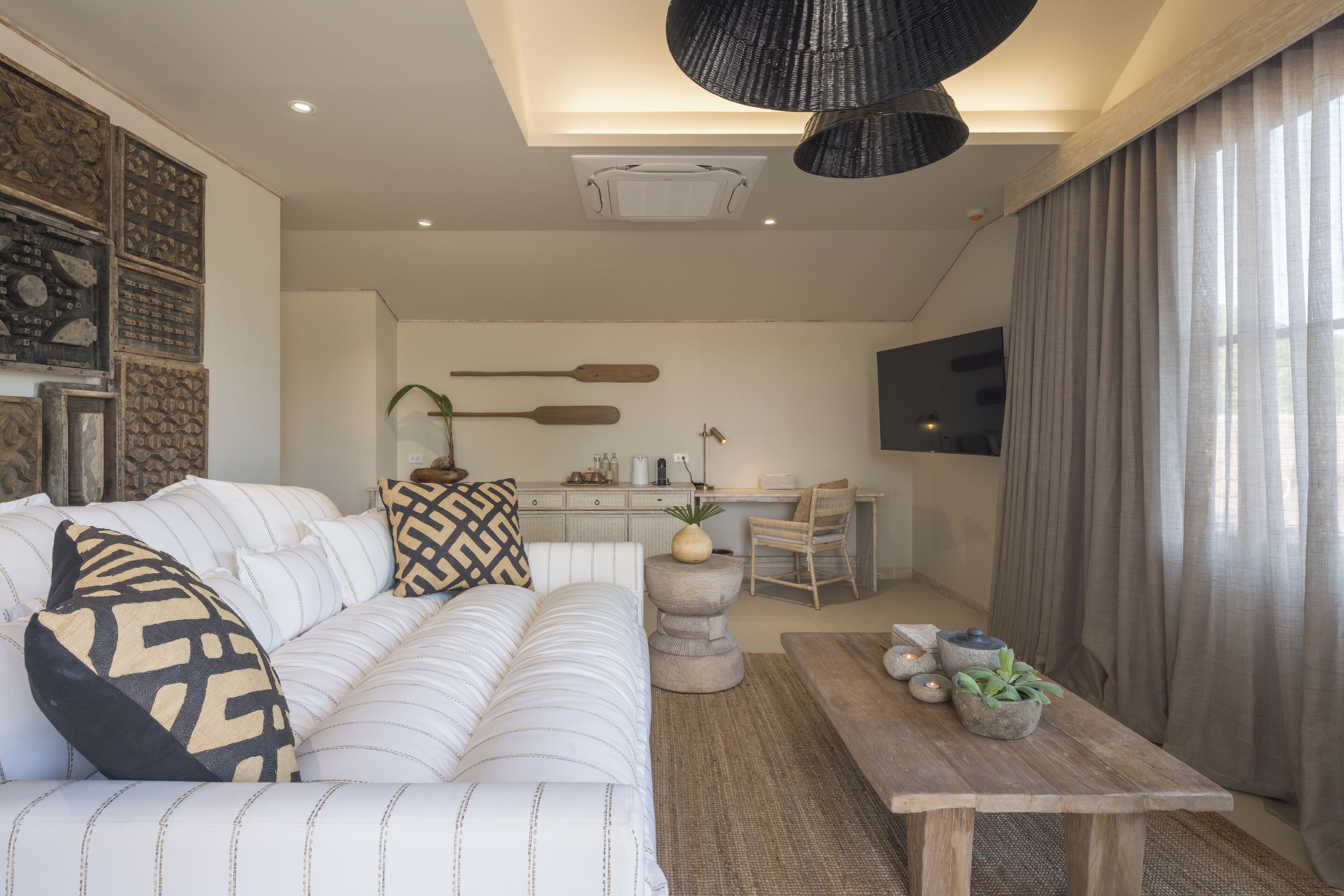 Un salon moderne avec un canapé, une table basse et des coussins décoratifs. On aperçoit à l’arrière-plan un coin cuisine avec une table à manger et des chaises.