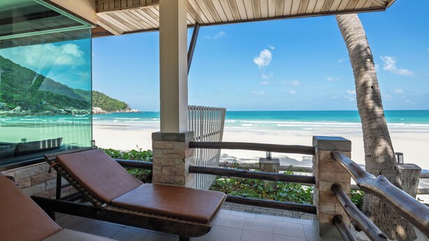 Vista a la playa desde un área techada con sillas de descanso y barandilla.