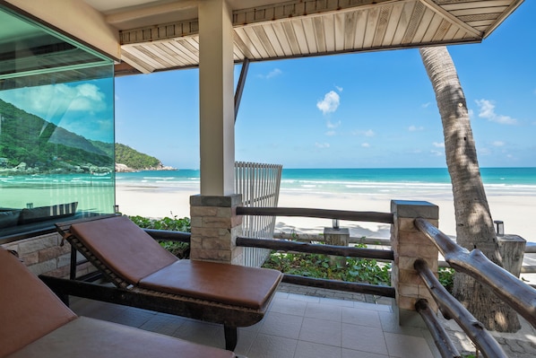 A beach view from a covered area with lounge chairs and a railing.