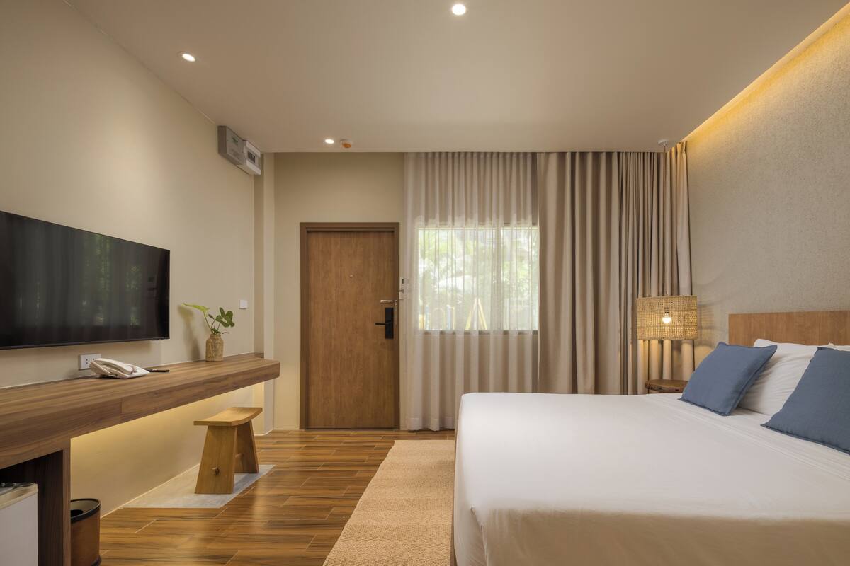 Een moderne hotelkamer met een groot bed, een flatscreen televisie aan de muur, een houten nachtkastje met een lamp en uitzicht op het omliggende landschap.