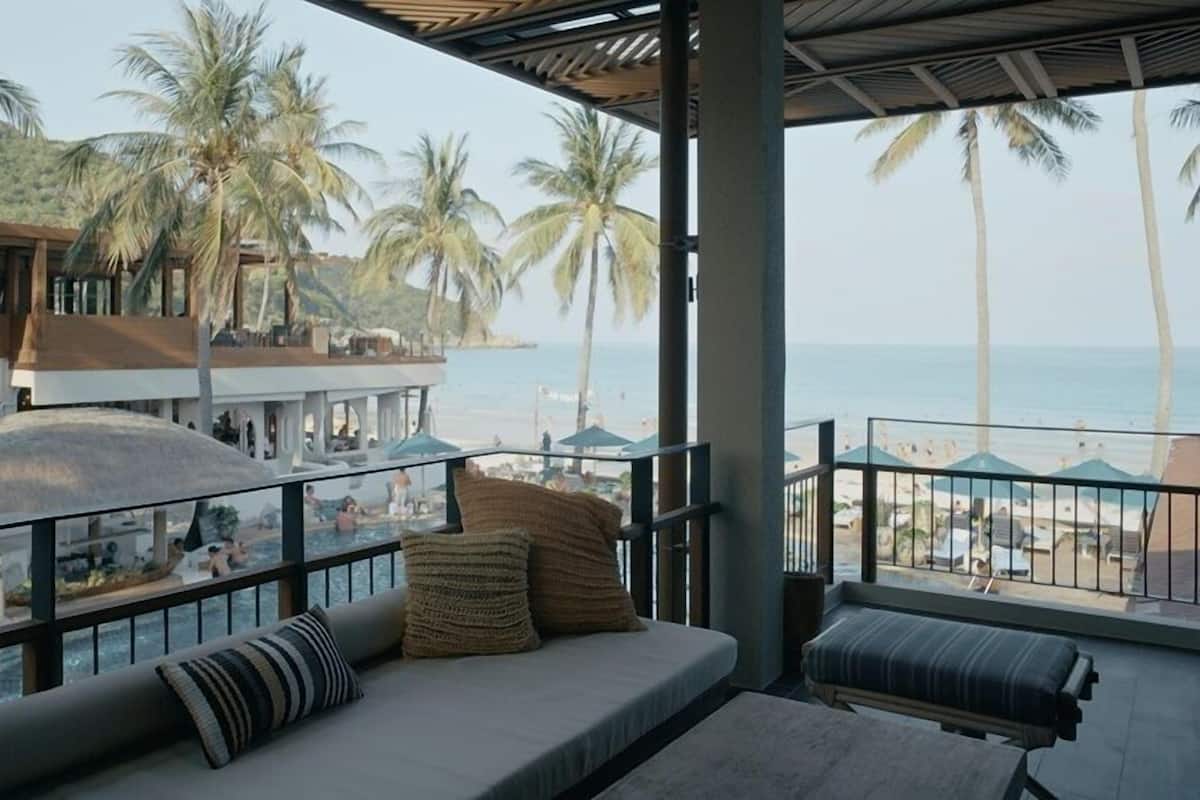 Een balkon met uitzicht op het strand, palmbomen en een zwembad.