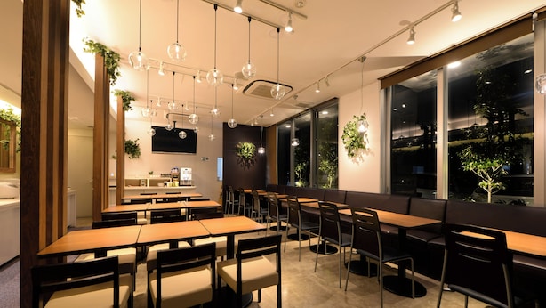 A restaurant with multiple tables and chairs, large windows, and hanging plants. - Vessel Inn Hiroshima Station (Hiroshima)