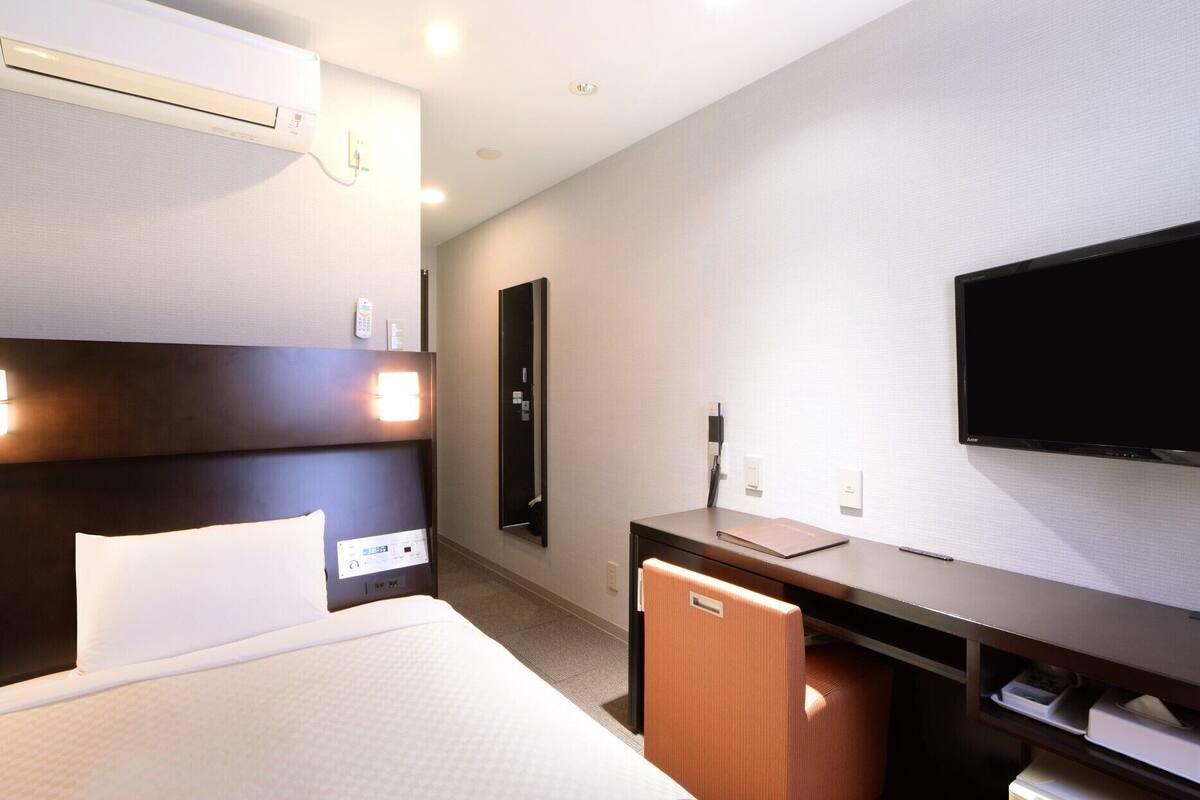 Habitación de hotel con cama, mesita de noche, televisor y aire acondicionado instalado en la pared.