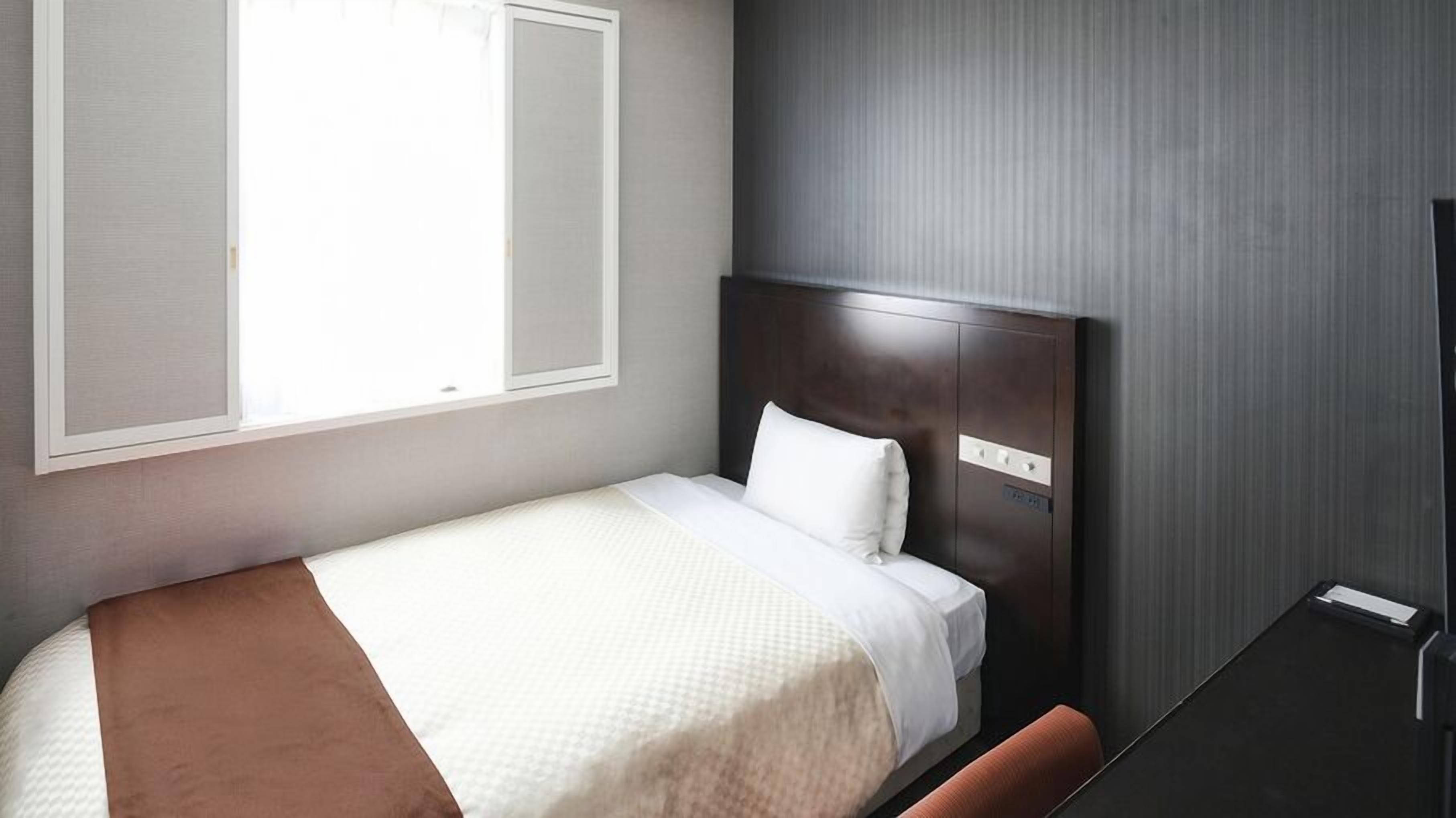A single bed with a headboard, a bedside table, and a window with blinds.