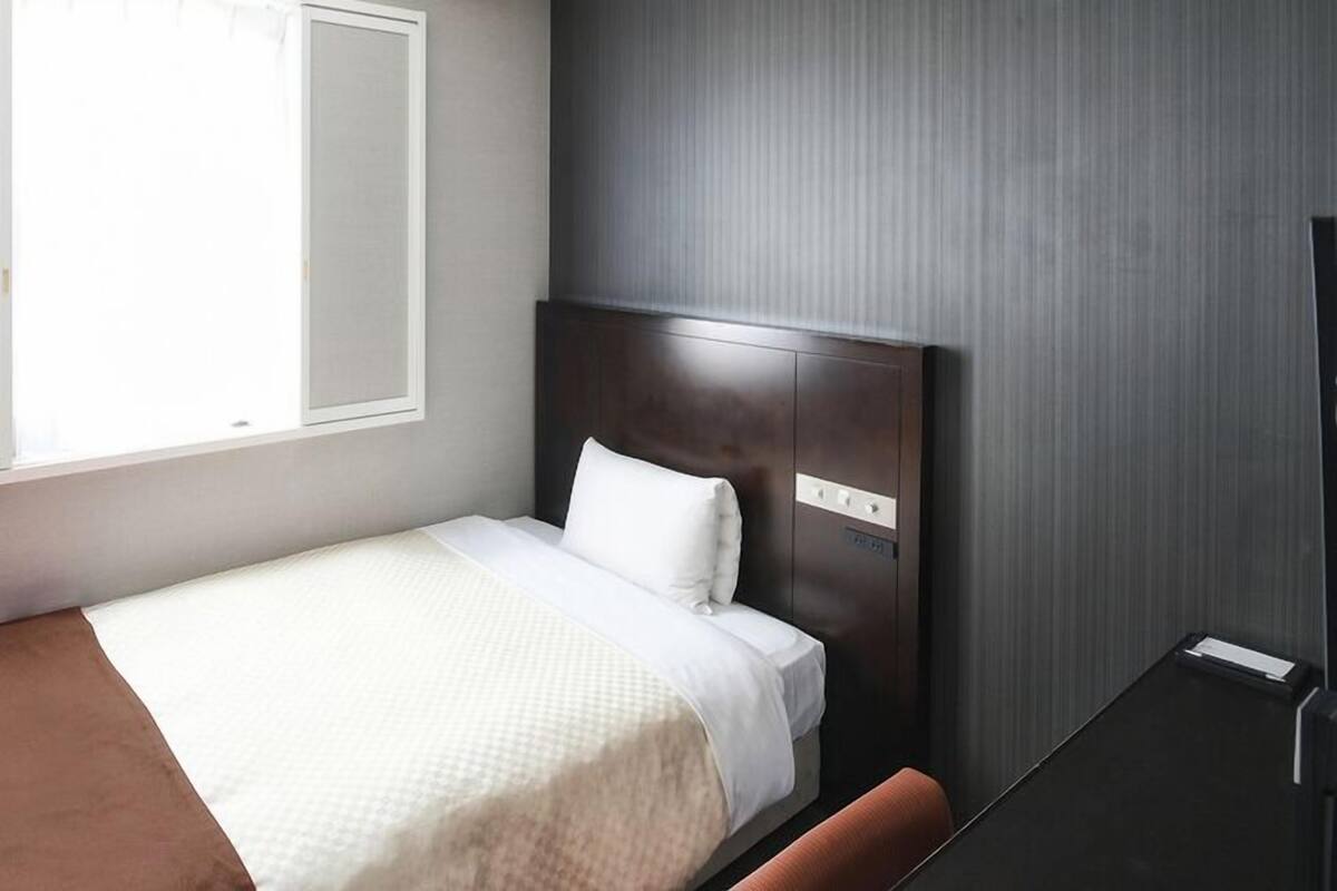 Una cama individual con cabecera, una mesita de noche y una ventana con persianas.