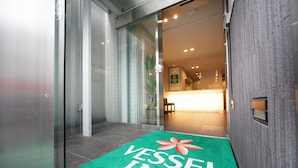A hotel entrance with a green carpet reading "VESSEL INN" and a reception desk in the background. - Vessel Inn Hiroshima Station (Hiroshima)