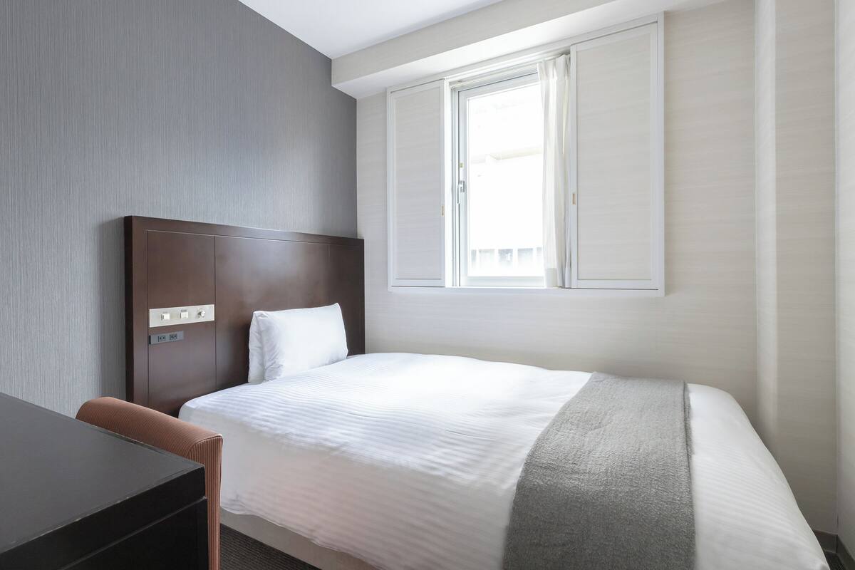 Una habitación de hotel con cama, escritorio y ventana.