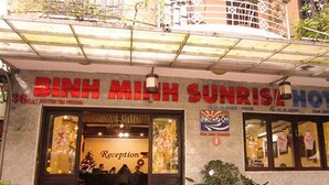 L’entrée d’un hôtel, avec un comptoir d’accueil, un sapin de Noël et une enseigne indiquant « Hôtel Binh Minh Sunrise ».