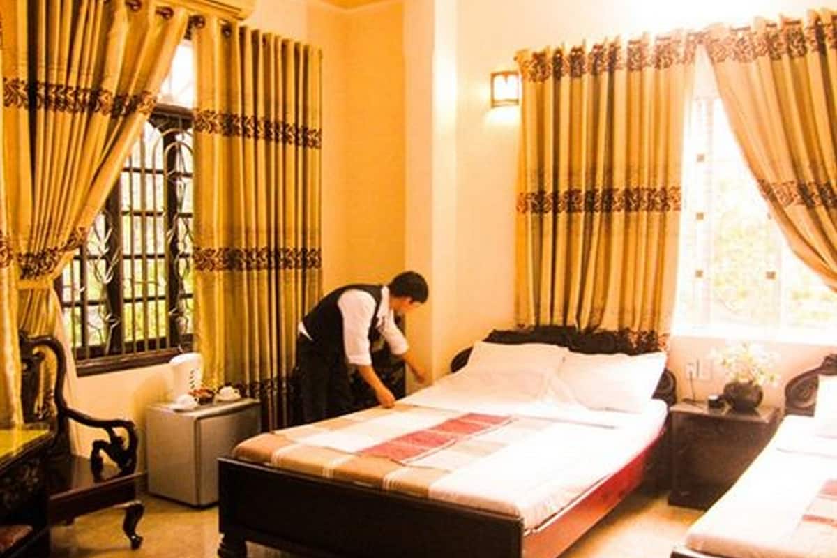 Une chambre d’hôtel avec deux lits, une fenêtre avec des rideaux, un bureau avec une lampe et une chaise.