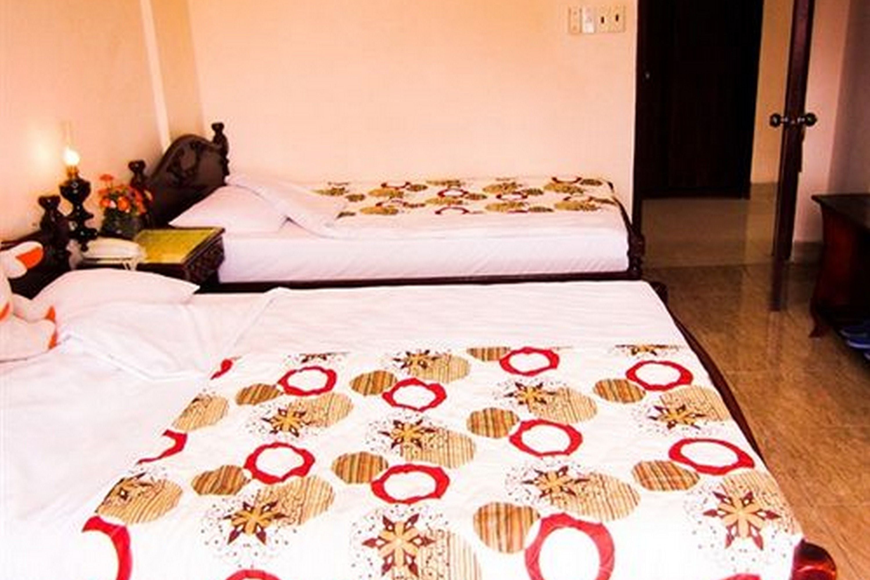 A hotel room with two beds, a nightstand with a lamp, and a door leading to another room.