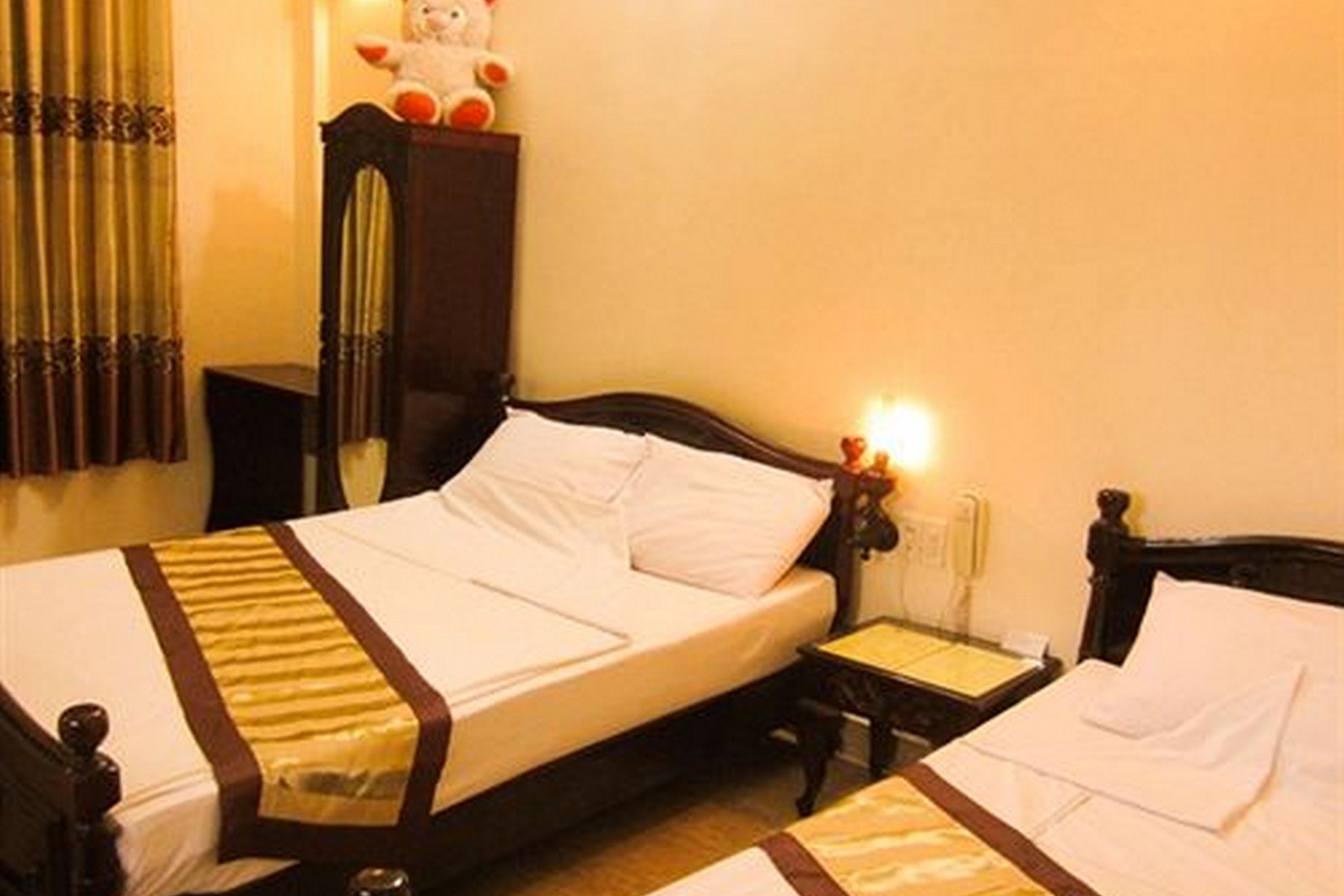 A hotel room with two beds, a nightstand, a lamp, and a stuffed toy on the dresser.