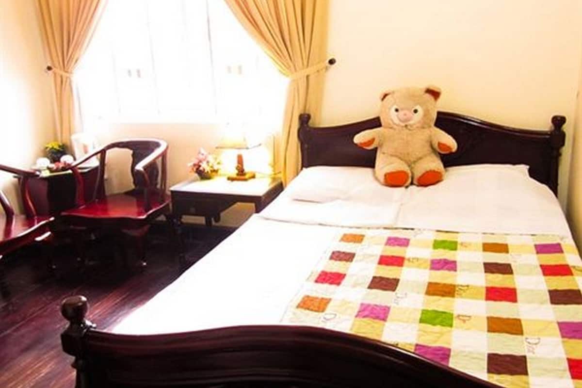 Un lit bien fait, agrémenté d’une couverture colorée, d’un ours en peluche moelleux posé sur les oreillers et d’une tête de lit en bois.