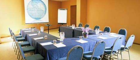 A conference room with long tables, chairs, a projector screen, and a globe on the wall.