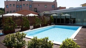 A rectangular swimming pool with a wooden deck surrounding it, a wooden fence, and potted plants. - Hotel Concorde (Camerano)