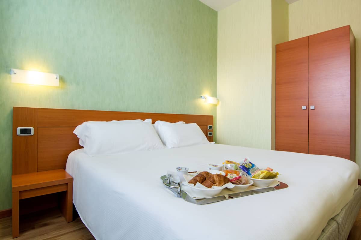 A hotel room with a bed, bedside table, and a tray with breakfast items.