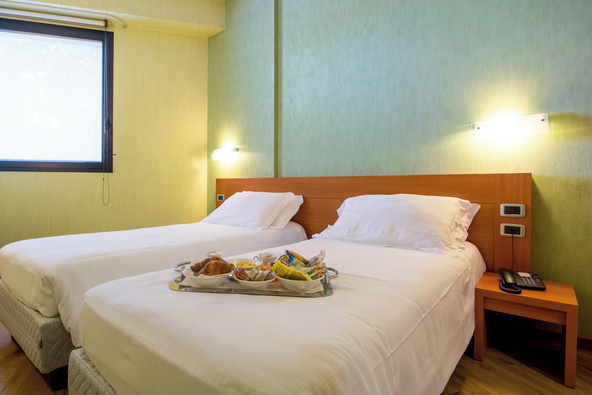 A hotel room with two beds, a tray of breakfast, a bedside phone, and a window.