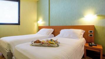 A hotel room with two beds, a tray of breakfast, a bedside phone, and a window.