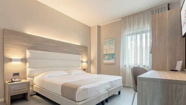 A modern hotel room with a large bed, bedside tables, a desk, and a chair. - Hotel Concorde (Camerano)