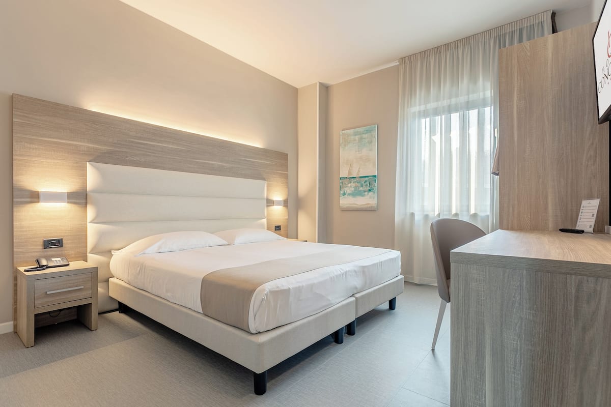 A modern hotel room with a large bed, bedside tables, a desk, and a chair.