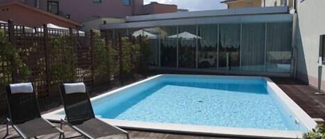 Piscina rectangular con cubierta de madera y dos sillones de descanso.