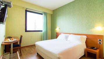 A hotel room with a bed, bedside table, chair, and a small table with breakfast items.