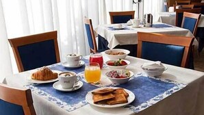A breakfast table set with croissants, coffee, orange juice, and a fruit bowl. - Hotel Concorde (Camerano)