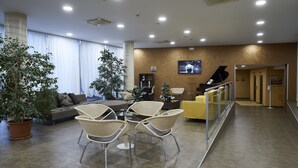 A modern lobby with a sofa, chairs, a piano, and potted plants. - Hotel Concorde (Camerano)