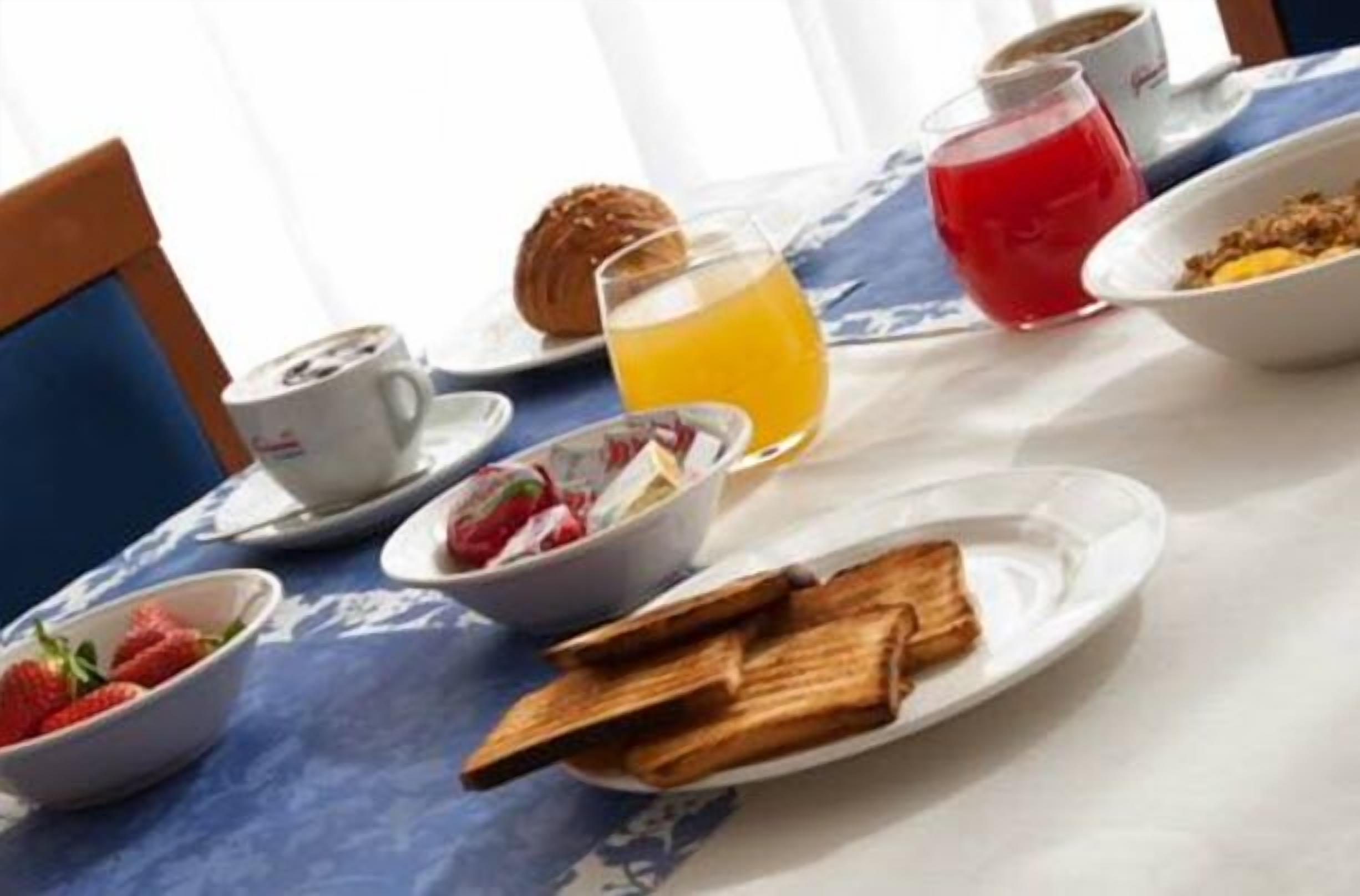Ein Frühstückstisch für zwei Personen, gedeckt mit Toast, Erdbeeren, Orangensaft, einem Muffin und einer Tasse Kaffee.
